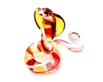 May include: A glass figurine of a cobra with a red, white and yellow striped body. The cobra is in a coiled position with its head raised and its hood expanded.