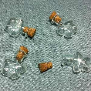 May include: Four small glass bottles with cork stoppers. The bottles are shaped like a paw print, a star, and two different paw prints. The bottles are clear glass and the corks are brown.