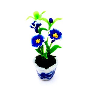 May include: A small blue and white ceramic planter with a blue and white flower arrangement. The flowers are blue with white edges and yellow centers.