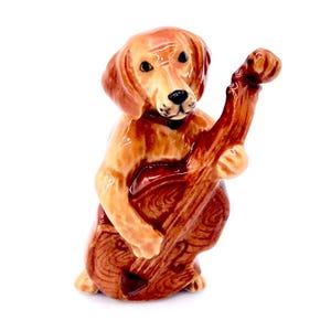 Könnte beinhalten: Eine Keramikfigur eines braunen Hundes, der eine braune Kontrabass spielt. Der Hund trägt ein schwarzes Halsband.