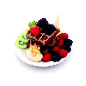 Könnte beinhalten: Ein Miniaturteller mit Waffeln, Kiwischeiben und Beeren. Die Waffeln sind gestapelt und mit Brombeeren und einer Erdbeere belegt. Scheiben grüner Kiwi und ein Klecks Sahne befinden sich ebenfalls auf dem Teller. Der Teller ist weiß.