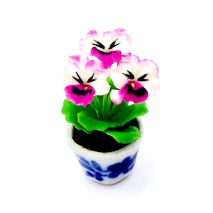 May include: A miniature ceramic potted plant with white and pink flowers. The pot is blue and white with a floral design.