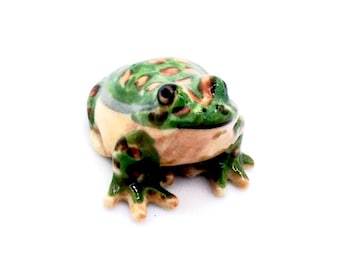 Op de afbeelding: Een keramieken kikkerfiguur met een gedetailleerd ontwerp. De kikker heeft een groen en bruin gevlekt patroon op zijn rug, met een lichtbruine buik en poten. De ogen zijn zwart en de kikker zit.