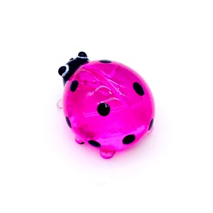 May include: A pink glass ladybug with black spots. The ladybug is a small, decorative figurine.