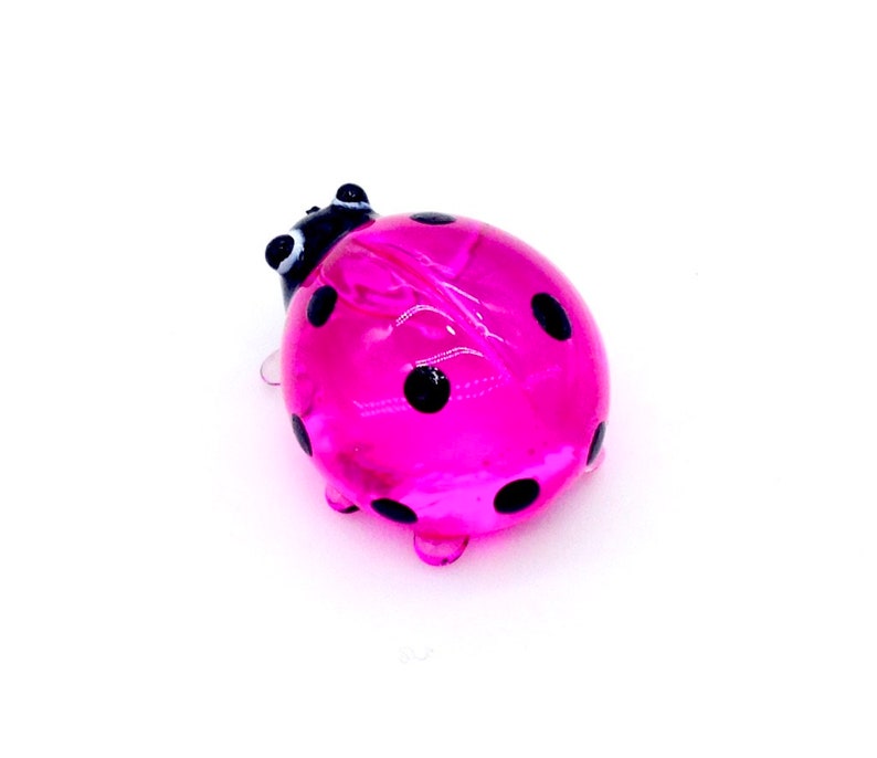May include: A pink glass ladybug with black spots. The ladybug is a small, decorative figurine.