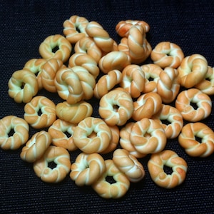 Könnte beinhalten: Ein Haufen kleiner, gedrehter, brotartiger Ringe, die an Mini-Bagels erinnern, in hellbrauner Farbe.