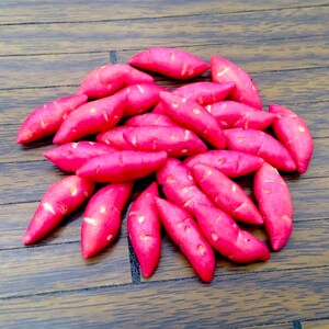 Op de afbeelding: Een stapel roze zoete aardappelen op een houten oppervlak.