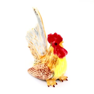 May include: A ceramic rooster figurine with a yellow body, brown and white tail feathers, and a bright red comb and wattle.
