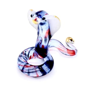 May include: A glass figurine of a cobra with blue, red, and white swirling patterns. The cobra is in a coiled position with its head raised and its hood expanded.