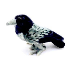 Może przedstawiać: Mała ceramiczna figurka kruka z czarnymi i szarymi detalami. Kruk siedzi ze złożonymi skrzydłami i pochyloną głową.