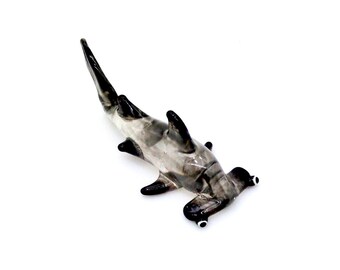 May include: A glass figurine of a hammerhead shark with a black and gray color scheme. The figurine is detailed with realistic features, including the hammerhead's distinctive head shape and eyes.