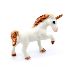 May include: A white porcelain unicorn figurine with brown mane and tail. The unicorn is standing on its hind legs with its front legs raised.