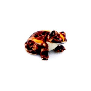 May include: A small ceramic frog figurine. The frog has a brown and orange spotted pattern with white accents on its belly and a yellow stripe on its back. The figurine is set against a white background.