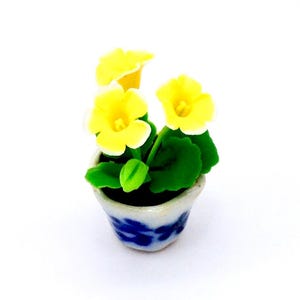 May include: A miniature ceramic flower pot with yellow and white flowers and green leaves. The pot is decorated with blue and white floral patterns.