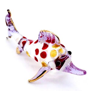 May include: A glass figurine of a swordfish with red and yellow polka dots on a white background. The figurine is made of glass and has a purple and gold finish.