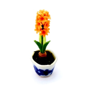 May include: A miniature orange hyacinth flower in a blue and white ceramic pot. The flower is made of polymer clay and is a realistic representation of a real hyacinth.