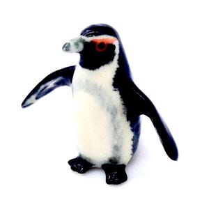 Könnte beinhalten: Eine kleine Keramik-Pinguin-Figur mit schwarzen und weißen Markierungen. Der Pinguin hat ein rotes Auge und einen schwarzen Schnabel.