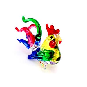 May include: A colourful glass rooster figurine with a red comb, yellow body, green wings, and a multi-coloured tail.