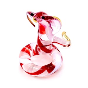 May include: A glass cobra figurine with red and white stripes. The cobra is coiled, with its head raised and hood flared. The figurine has gold accents on the hood and eyes. The snake is a decorative item.