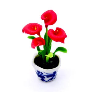 May include: A miniature potted plant with red calla lily flowers in a blue and white ceramic pot. The plant is made of polymer clay and is ideal for dollhouses or miniature gardens.