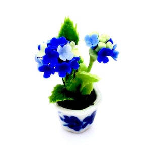May include: A miniature potted hydrangea plant with vibrant blue and white flowers. The plant has green leaves and is set in a small white pot with blue floral designs. The overall aesthetic is delicate and charming, suitable for dollhouses or miniature displays.