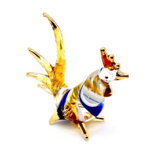 May include: A small glass rooster figurine with a gold and white striped body, blue accents, and a gold comb.