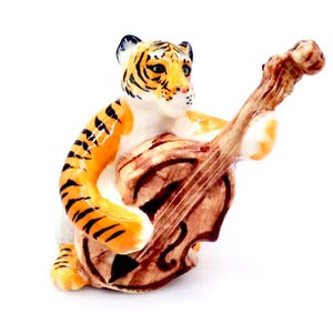 Könnte beinhalten: Eine Keramikfigur eines Tigers, der Geige spielt. Der Tiger hat orange und schwarze Streifen mit weißem Bauch und Gesicht. Die Geige ist braun mit einem hellen Hals und Bogen.