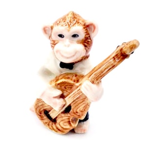 Könnte beinhalten: Eine Keramikfigur eines Affen, der ein weißes Hemd und eine schwarze Fliege trägt und eine braune Gitarre spielt.