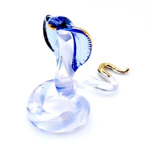 May include: A glass figurine of a cobra with a blue and gold body. The cobra is in a coiled position with its head raised.