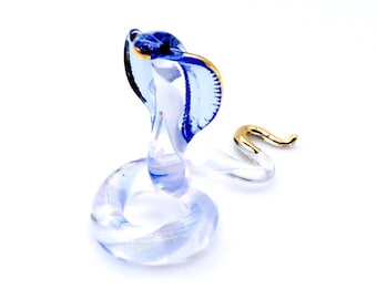May include: A glass figurine of a cobra with a blue and gold body. The cobra is in a coiled position with its head raised.