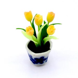 May include: A miniature potted plant with five yellow tulips. The tulips have orange tips and green stems and leaves. The small white pot has a blue floral design.