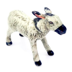 May include: A small, white ceramic donkey figurine with black hooves and a black nose. The donkey has a gray and white spotted coat and is standing on all four legs.