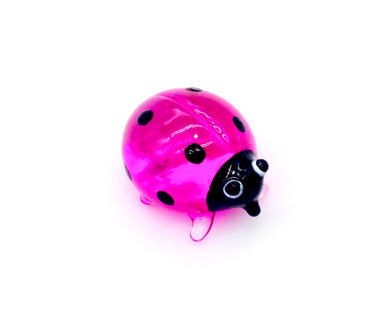 May include: A pink glass ladybug with black spots and black eyes. The ladybug is a small, decorative figurine.