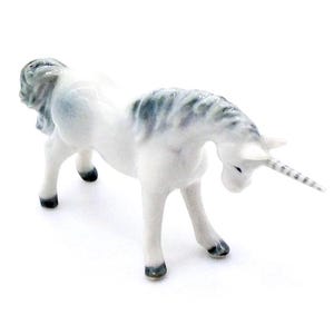 May include: A ceramic unicorn figurine in white with gray and black accents. The unicorn has a striped horn and is posed with its head lowered. The figurine's hooves and mane are detailed with gray and black.