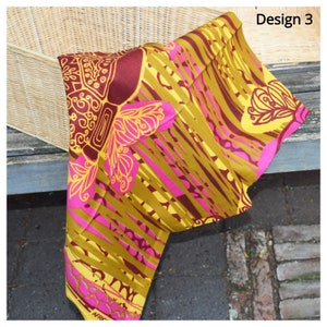 May include: A yellow, pink, and brown fabric with a geometric pattern. The fabric has a design of stylized flowers and leaves. The fabric is folded and draped over a wicker basket.