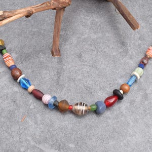 Könnte beinhalten: Eine farbenfrohe Perlenkette mit Perlen in verschiedenen Formen und Größen. Die Perlen sind in Rot-, Blau-, Braun- und Weißtönen gehalten. Die Kette ist an einer silbernen Kette befestigt und ein einzigartiges Schmuckstück.