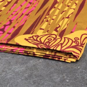 May include: Folded fabric with a vibrant pattern. The design features a combination of yellow, brown, and pink hues. The fabric has a repeating pattern of vertical lines and floral motifs, creating a visually striking textile.