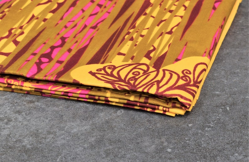 May include: Folded fabric with a vibrant pattern. The design features a combination of yellow, brown, and pink hues. The fabric has a repeating pattern of vertical lines and floral motifs, creating a visually striking textile.