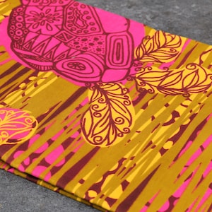 May include: Close-up of a folded fabric with a repeating pattern. The design features large, stylized floral and geometric shapes in shades of pink and brown, set against a mustard yellow background with diagonal stripes.