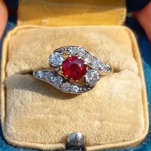 May include: A ring with a large red ruby surrounded by smaller diamonds set in a gold band.