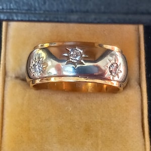 May include: A gold band ring with three small diamonds set in a starburst design.