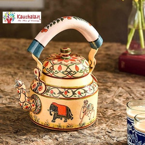 May include: Hand-painted metal tea kettle with a white base and colorful floral and animal designs, including an elephant and a camel. The kettle has a white handle with blue accents. The text "Kaushalam The Flow of Creativity" is visible on the image.