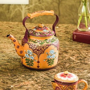May include: An orange-colored, hand-painted teapot with a matching small creamer. The teapot features a floral design with blue and white flowers, a wooden handle, and a purple rim. The creamer has a similar design. The teapot is approximately 8 inches tall.
