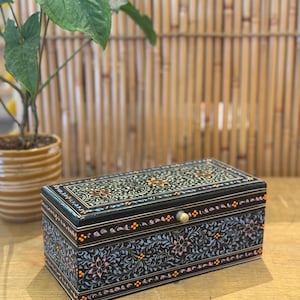 May include: A black wooden box with a floral design painted on the lid and sides. The box has a brass knob and is sitting on a wooden surface.