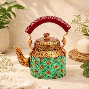 Puede incluir: Una tetera de metal con una base de color verde vibrante adornada con patrones florales naranjas y espirales negras. La sección superior es dorada con detalles pintados intrincados, mientras que el asa arqueada es roja con acentos decorativos blancos y negros.