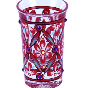 May include: A clear glass tumbler featuring hand-painted red floral patterns with teal accents and black outlines. The design includes a geometric diamond lattice structure and small, circular purple rhinestones embedded along the exterior surface.