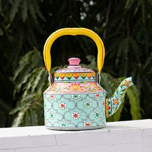 Peut inclure: Une théière en métal avec une anse jaune vif et un corps vert menthe clair orné d'un motif floral répétitif blanc et rouge. Le couvercle est rose avec des accents orange et verts, et le bec verseur présente un motif floral coloré.
