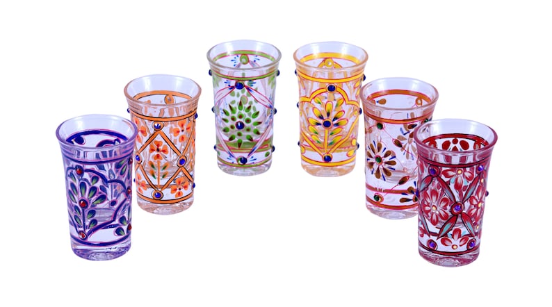 May include: A set of six clear glass tumblers, each featuring distinct hand-painted floral and geometric patterns in vibrant colors including purple, orange, green, yellow, and red, accented with small raised dots along the exterior surface.