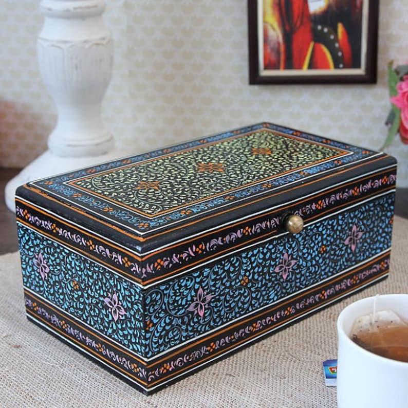 May include: A black wooden box with a decorative floral design painted in blue, green, yellow, and pink. The box has a brass knob on the lid.