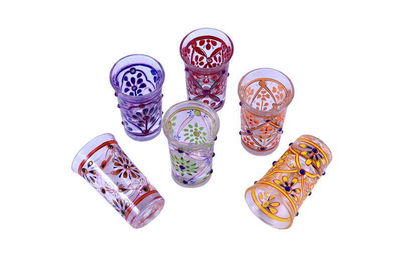 May include: A set of five clear glass tumblers, each decorated with distinct hand-painted floral and geometric patterns in vibrant colors including red, orange, purple, green, and yellow, featuring raised paint details along the exterior.